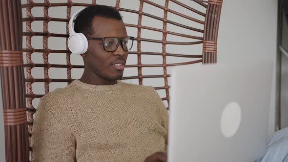 Man in Headphones Works in Laptop Swinging in Basket Chair