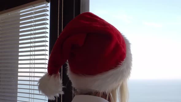 rear view, a young beautiful woman in a Santa Claus hat looks out the window