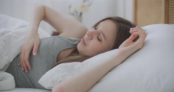 Sick Woman Sleeping in Bed Under Blanket. Woman Covering Her Ears with a Duvet. Young Woman