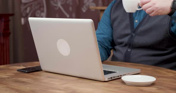 Man Drinks a Bit of Espresso While Working on His Laptop