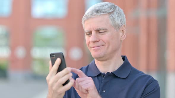 Outdoor Portrait of Cheerful Middle Aged Man Using Smartphone