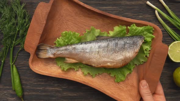 Hands are Placing a Wooden Plate with a Delicious Juicy Grilled Red Char Fish