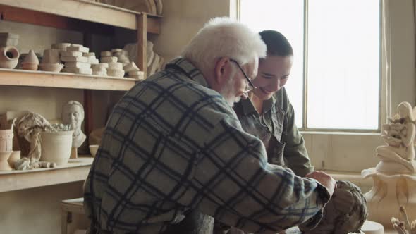 Elderly Sculptor Teaching Young Woman How to Create Clay Head