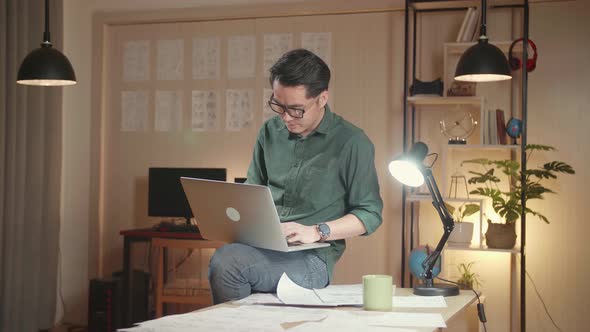 Creative Designer Sits On His Desk Holds Laptop On The Knees And Working On The Project