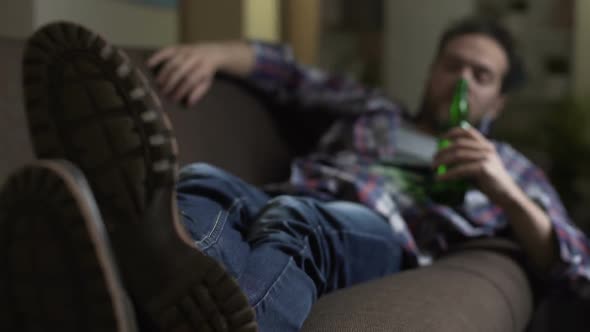 Wasted Guy Lying on Sofa, Drinking up Beer from Bottle, Dozing Off, Alcoholism