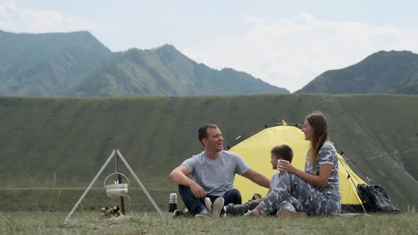 Happy Family with a Child Laughing on Campsite Near a Tent with a Bonfire