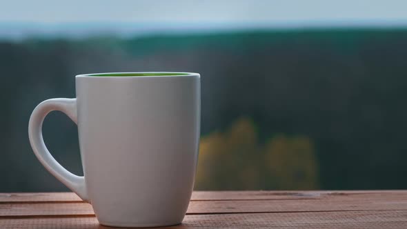 Cup of Hot Tea or Coffee Stands By an Open Window and Emits Steam