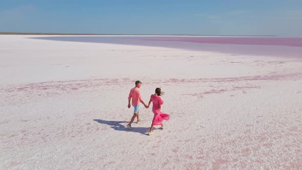 Aerial Drone Footage of Happy Young Couple in Pink Wear Having Fun and Joyfully Running on White
