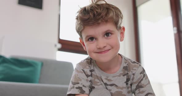 Close Up of a Little Boy Drawing on the Floor Who Looks to the Camera and Smiles Shyly Grey Sofa and