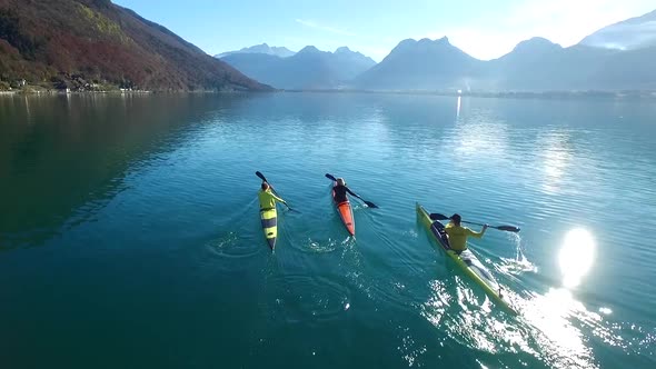 Three kayakers paddle in a scenic mountain lake.