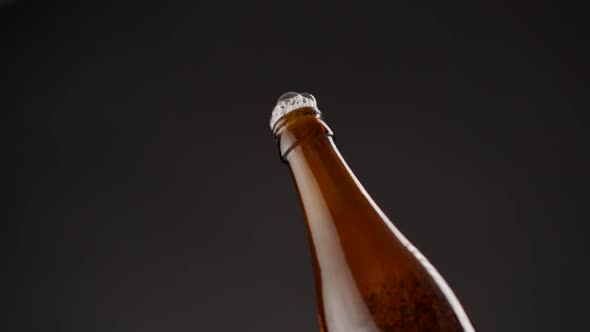 Foam comes out of a bottle of beer on a black background