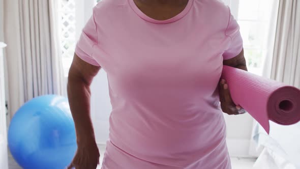 Portrait of senior african american woman holding yoga mat smiling at home