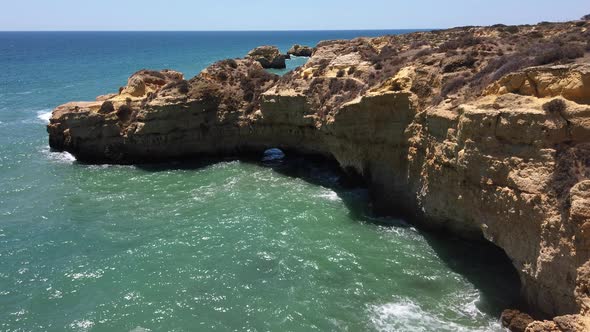 Ocean waves crash against limestone yellow cliffs in Algarve, Portugal, wide.