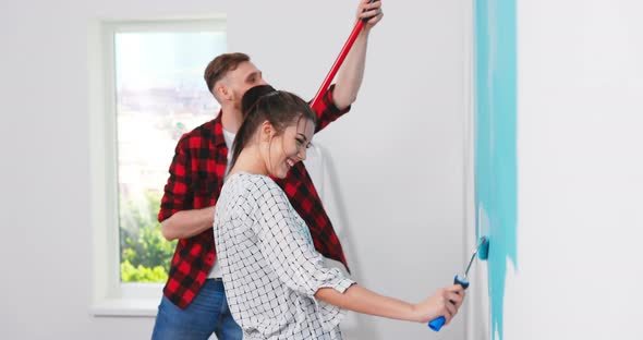 Cute and Beautiful Young Caucasian Woman Painting Walls in the Apartment in Blue Color with