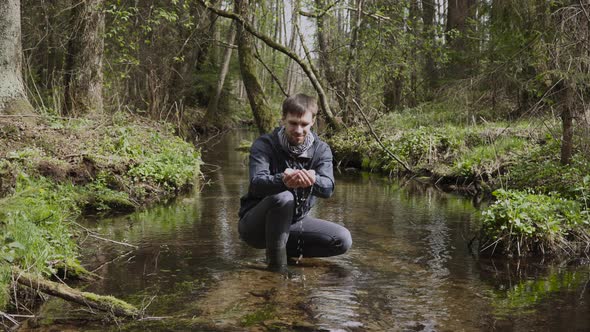 Man Squats in Stream in Forest