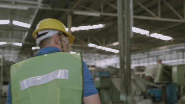 Back view of engineer man in hard hat walking and checking machine with professional in factory.