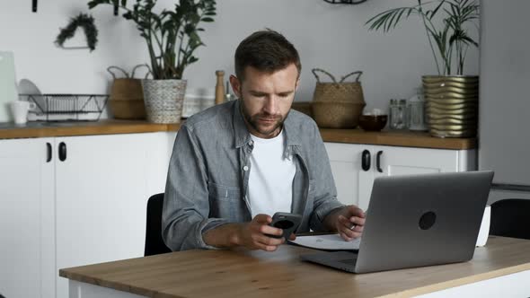 Young adult man work at home office, using desktop computer and smartphone. Work from home