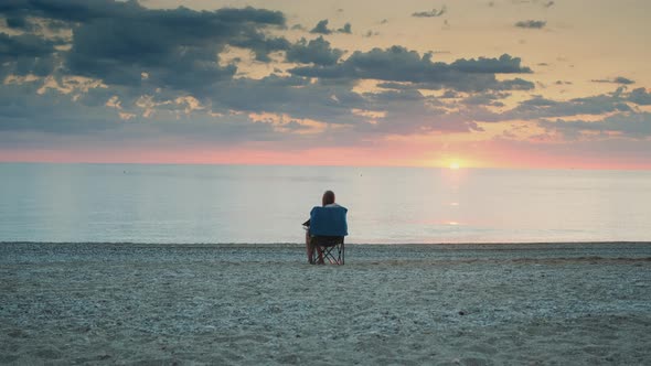 Full Shot of Woman Admiring Sunset on the Sea Sitting in Folding Tourist Chair