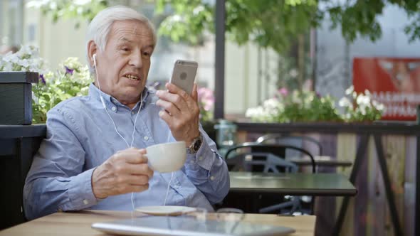 Senior Man Video Conferencing on Smartphone in Cafe