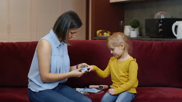 Mother Measuring, Monitoring Oxygen Saturation with Digital Pulse Oximeter of Her Daughter at Home