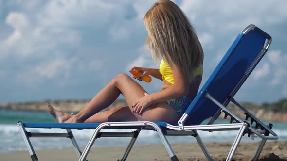 Girl Is Lying on a Lounger on the Beach and Use a Sunburn Spray on Her Body To Not Get Burnt