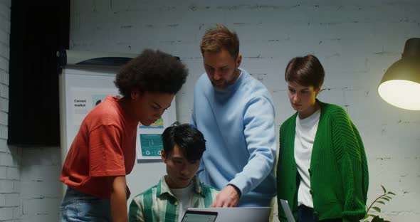 A Group of People Stand Near Workplace of Their Colleague and Look at His Laptop