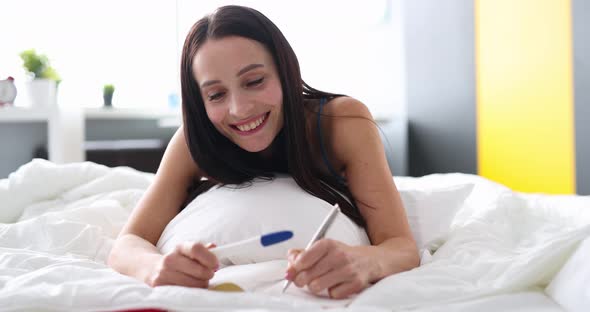 Joyful Woman Holding Pregnancy Test While Lying in Be Closeup