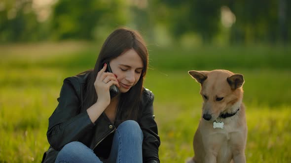 Attractive Girl Talking on the Smartphone While Walking with a Dog in the Park.