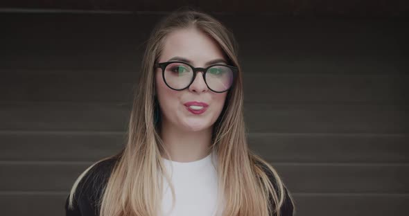 Stylish Teenager with Makeup in Glasses Inflates Chewing Gum Into the Camera