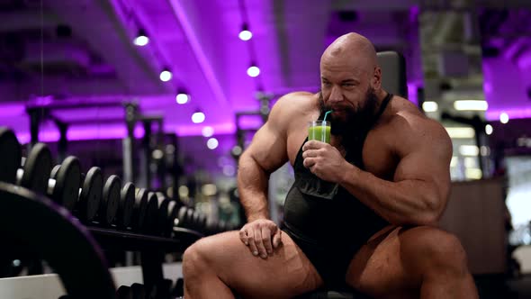 A Mature Male Bodybuilder Drinks an Energy Drink Made of Fruit During a Break in the Gym