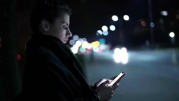 Lonely Woman Typing on Smartphone City at Night Sitting on a Bench Near Boulevard