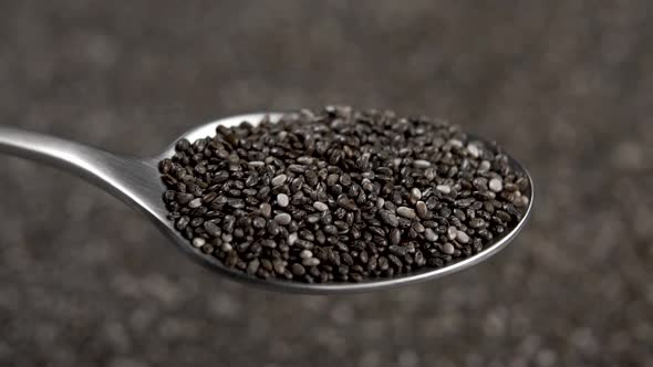 Chia seeds fill a metal spoon and fall into a heap in blur. Background rotation