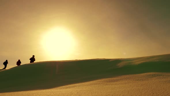 Team of Travelers Follow Each Other Along Snow Ridge Against Backdrop of Yellow Sunset. Coordinated