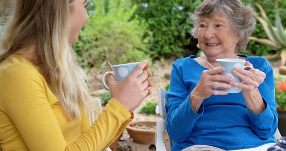 Senior woman and young girl having coffee in homeyard 