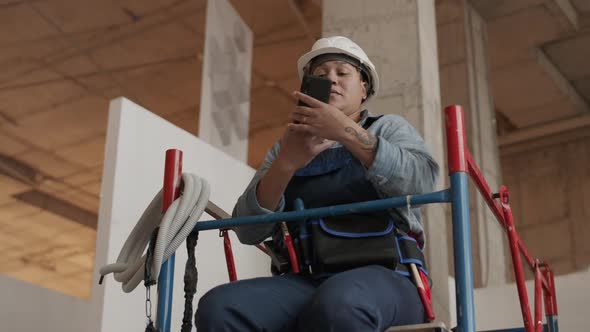 Worker Sitting on Scaffolding Using Smartphone
