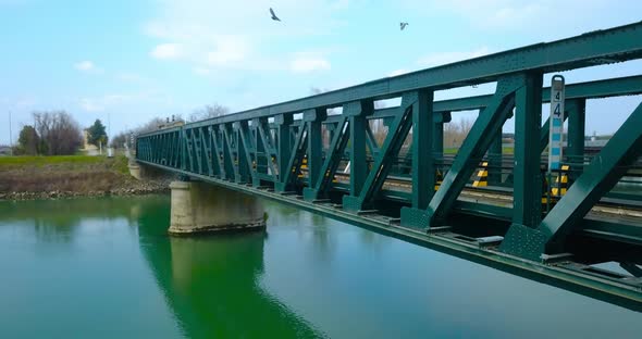 A Green Steel Bridge Over the River with Birds Flying in Front