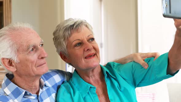 Senior couple taking selfie from mobile phone in the living room