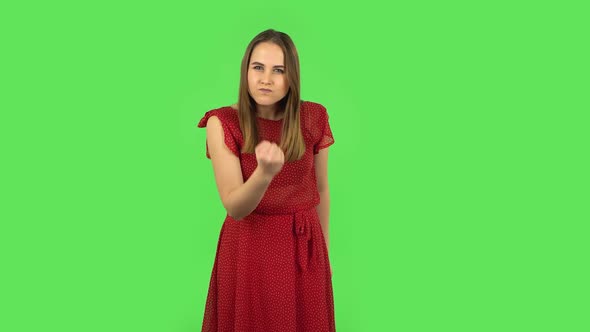 Tender Girl in Red Dress Is Threatening with a Fist. Green Screen