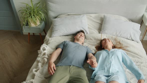 Happy Couple Girl and Guy Falling on Bed Holding Hands Lying Smiling Relaxing