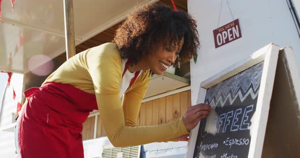 African american woman wearing apron writing on food menu slate board of the food truck