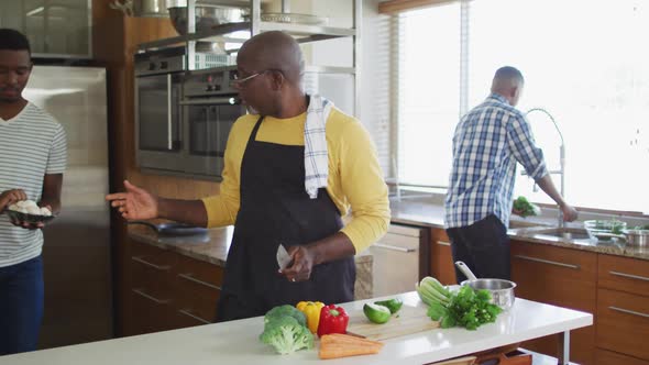 African american senior father and two adult sons standing in kitchen cooking dinner and talking