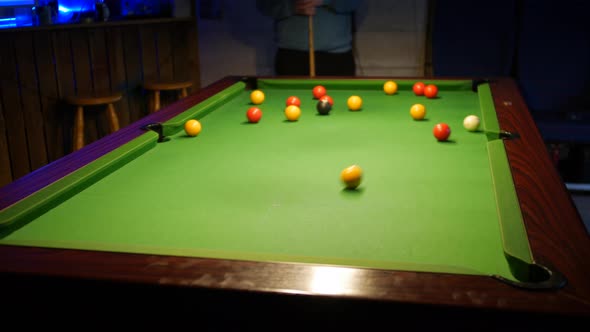 A man breaking the balls in a game of pool. The white ball is hit on the break in a pub bar.