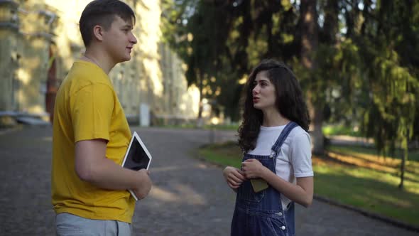 Confident Positive Young Caucasian Woman Talking with Man Standing at College Campus Outdoors