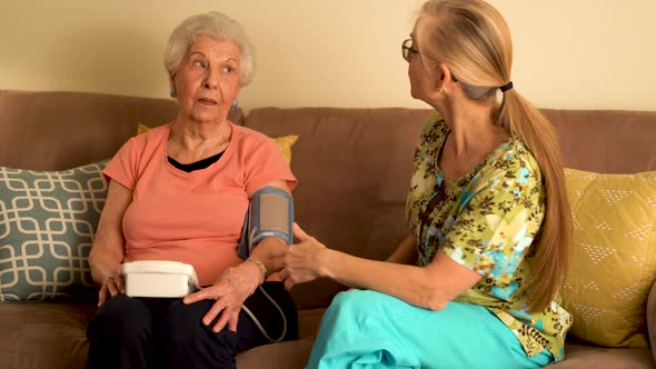 Home healthcare nurse and elderly woman taking blood pressure with a machine.