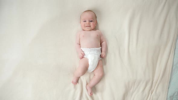 Top View of Little Baby Boy in Diapers Lying on Soft White Blanket on Bed