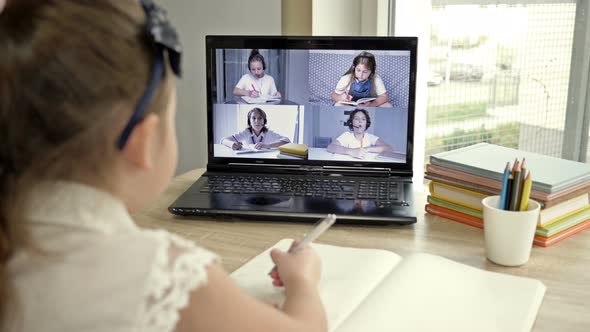 Schoolgirl in Front of a Laptop Screen Performs School Assignments. On the Screen Are Classmates