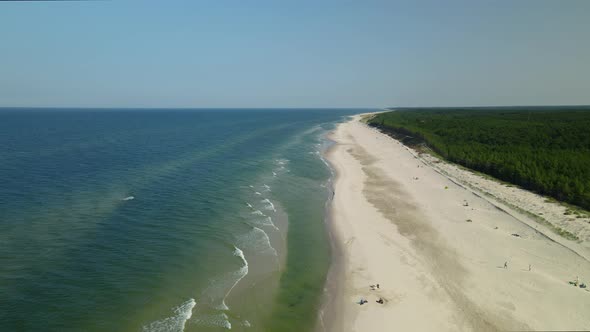 Flying forward along the white-sand beach line in Osetnik, Poland, daytime cloudless sky