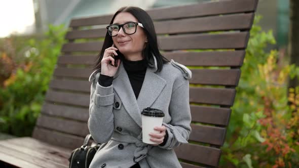 Woman in Dinner Break in Working Day Sitting Outdoors with Cup of Coffee and Chatting By Cell Phone