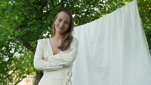 Young Woman Crosses Her Arms and Looks at the Camera Against the Background of Clean Bed Linen