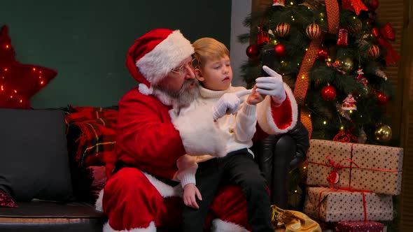 Santa Claus with a Child Sitting on His Lap Communicate Via Video Call on a Smartphone